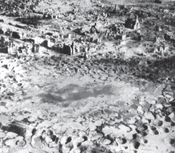 A black-and-white aerial photograph of a war-torn landscape, showing the ruins of buildings and the ground extensively pockmarked with water-filled craters.
